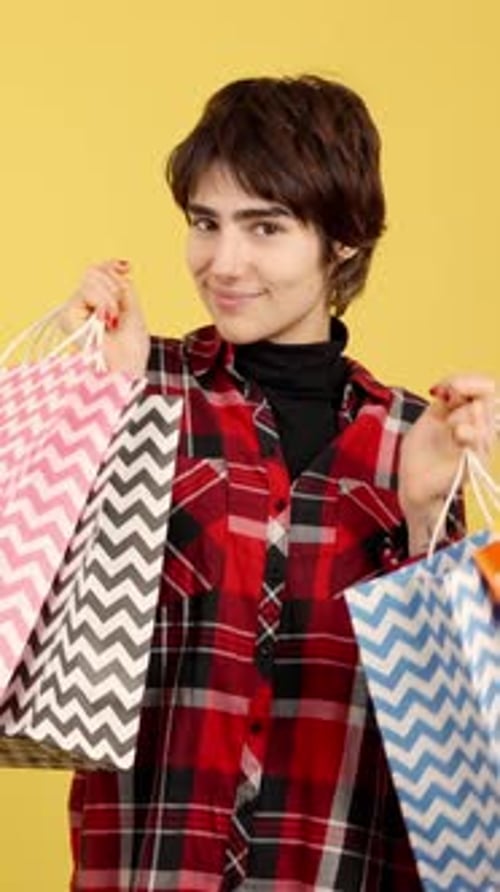 Persona andrógina feliz que sostiene muchas bolsas de compras