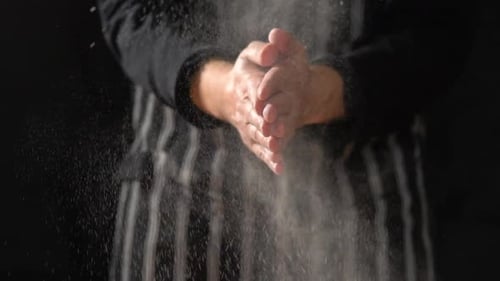 MCU SLOW MOTION: Männlicher Koch mit Schürze klatscht die Hände zusammen, Mehl fliegt durch die Luft und reibt dann Han