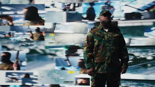 Man in Camouflage Standing Before Wall of Monitors