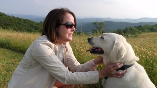 Medium shot of woman playing with white lab dog with mountain backdrop