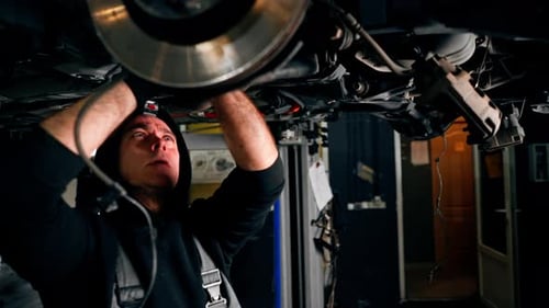 an Auto Mechanic at a Service Station Tightens the Bolts Under the Wheel with a Wrench