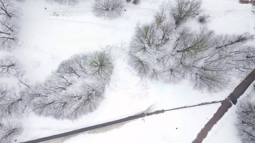 Aerial tracking shot above a city park and a residential building's yard covered in snow