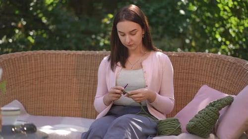 Woman Crocheting Yarn Outside on Wicker Couch