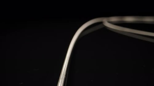 Metal strings from a guitar, rolled up lie on a black table. Dolly slider extreme close-up.