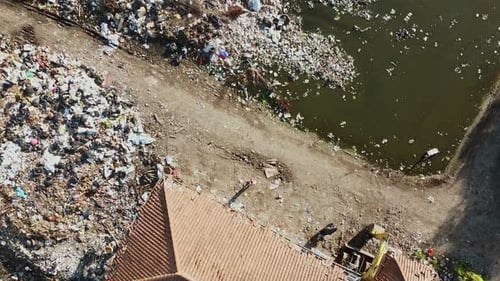 Aerial top view of a house with huge landfill pile of dump and trash beside near mangroves trees in