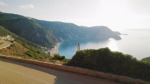 Woman stands overlooking a wide summer bay surrounded by cliffs in Kefalonia Greece