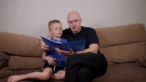 Father and Son Reading a Book on Sofa