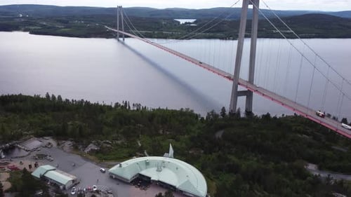 4K drone shot of a suspension bridge reaching over a vast lake, with cars and trucks driving over it