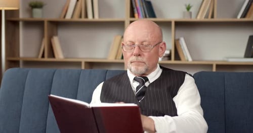 Senior Man Reading Book on Couch Indoors