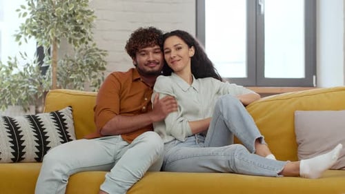Affectionate couple cuddle on bright yellow sofa indoors