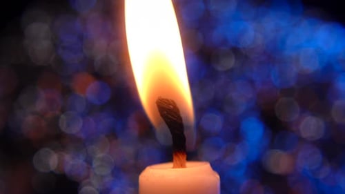 Illuminated Candle Flame Against Colorful Bokeh Background