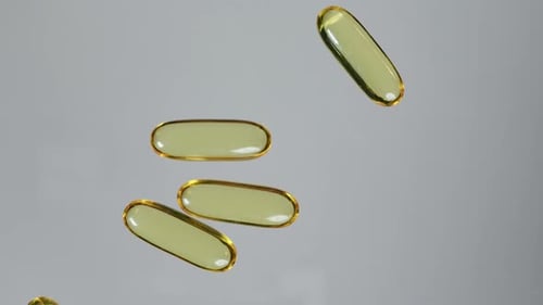 Yellow transparent capsule with fish oil or vitamin E, vitamin D tablet rolling into frame on flat