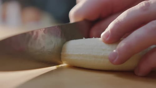 Person Slices a Banana on Cutting Board Close-Up