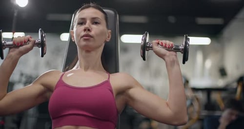 A Young Beautiful Brunette Girl in Sportswear is Exercising on a Machine in the Gym Doing Arm