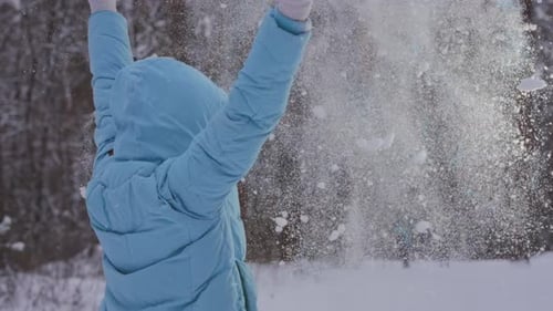 Caucasian Woman With Arms Raised Stands On Snowy Trail Surrounded By Tall Trees And Falling Snow