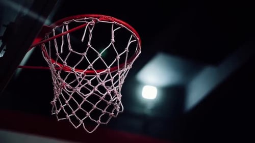 A basketball hits the basket in an indoor sports arena.
