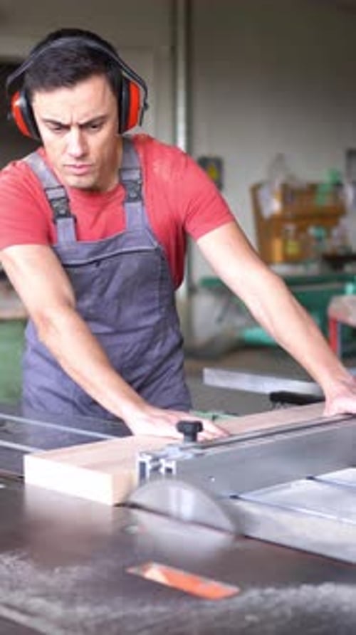 Woodworker Cutting Plank with Table Saw in Workshop