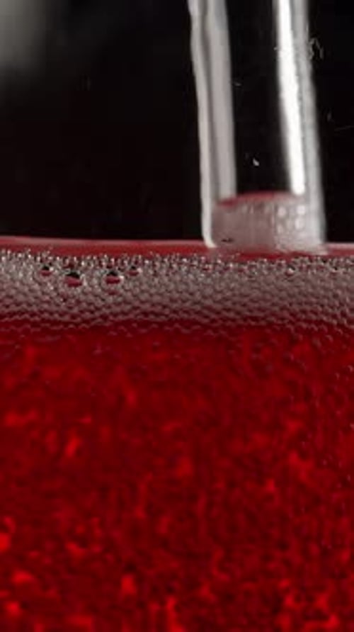Vertikales Video. Seifenblasen in einer Glasflasche mit roter Limonade, Macro. Auf einem schwarzen Hintergrund.