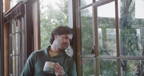 Caucasian man holding cup of coffee and looking out window at home, slow motion, slow motion