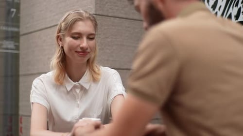 Caring Young Man Bringing Coffee to Summer Cafe Table Where Sitting Charming Blonde Girlfriend