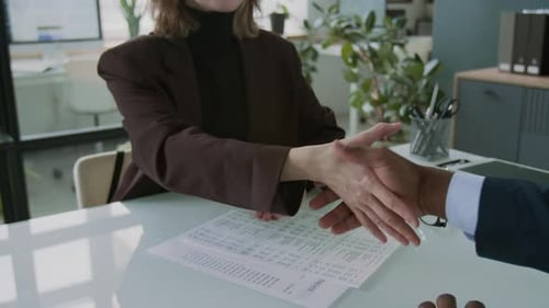 Woman Shaking Hands with Financial Advisor over Documents on Office Desk