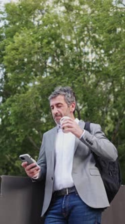 Man with Coffee Using Phone on City Street