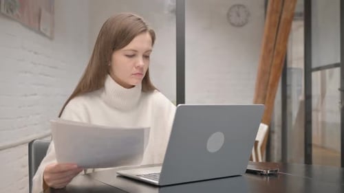 Woman Working on Laptop with Documents at Desk