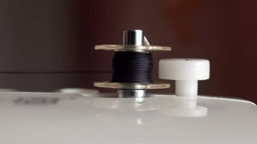 Closeup of Automatic Thread Winding on a Sewing Machine Bobbin Winding a Black Thread on a Small