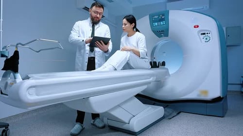 Doctor Talking to Patient Before Undergoing MRI Doctor Holding Tablet Patient Sitting at CT Scanner