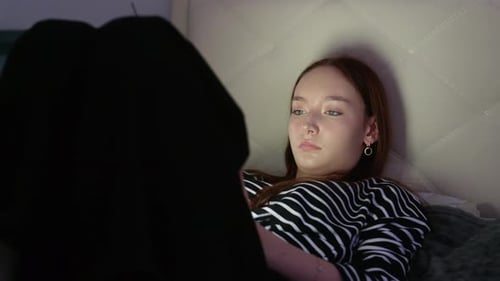 Young Woman Using Tablet Lying in Bed in the Dark