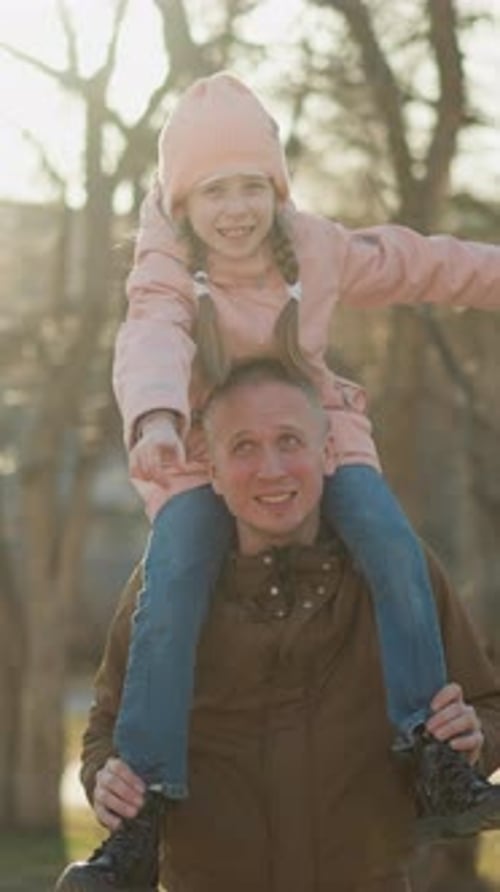 Joyful Girl Spreading Arms on Father's Shoulders in Sunlit Park