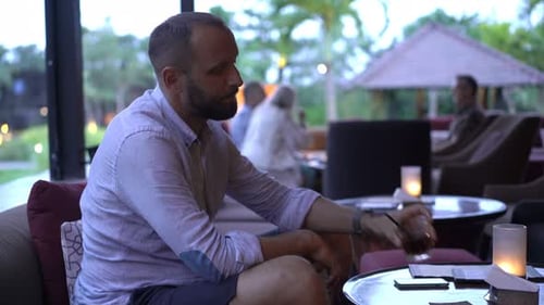 Young, Happy Man Drinking Cocktail Sitting In Garden In Cafe