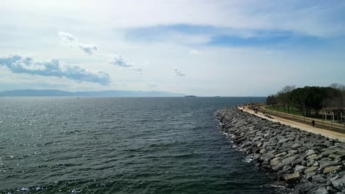 Park by the ocean with a rocky shore in summertime, drone backwards shot