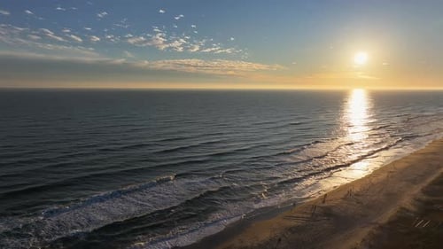 Vibrant aerial footage of the coastline during sunset, with waves meeting the shore.