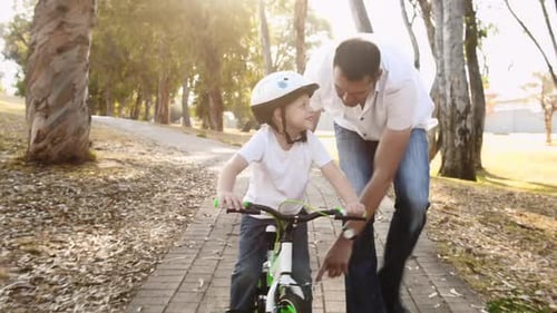 Father teaches son to ride bike on park pathway in sunny outdoors with safety helmet