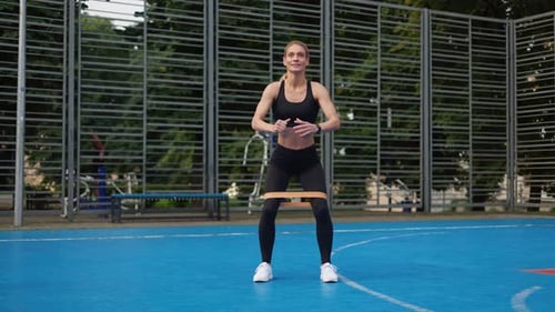 Woman Doing Squats with Resistance Band on Court