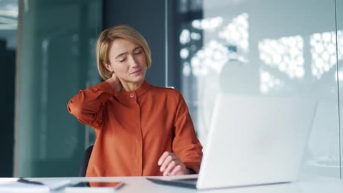 Woman Massaging Neck at Desk in Office