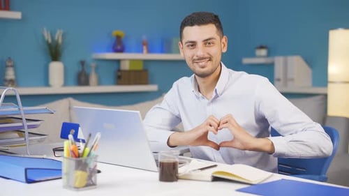 Home office worker man makes heart symbol looking at camera.