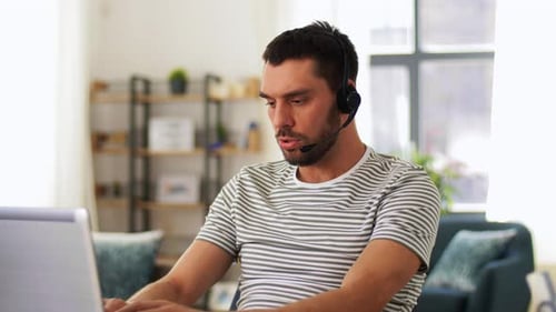 Man Working On Laptop Wearing Headset At Home