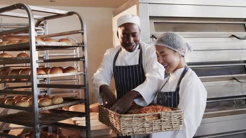 Portrait of happy diverse bakers working in bakery kitchen, holding fresh bread in slow motion