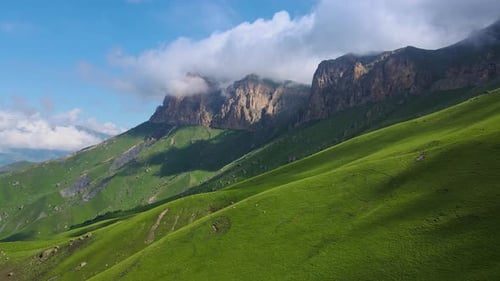 Ein grüner, grasbedeckter Berg mit blauem Himmel und Wolken im Hintergrund