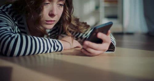 Young Woman Lying near Smartphone on Floor