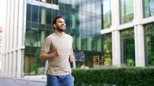 Young adult male runner jogging along a park alley on a city street. Handsome active man