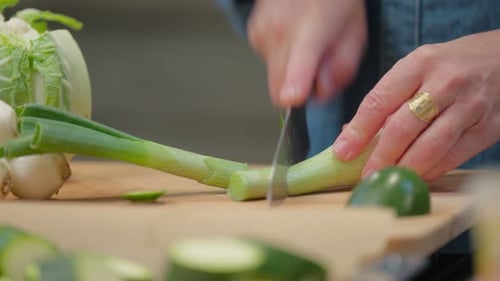 Woman preparing vegetables by cutting scallions on board