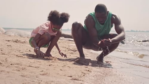 Father and Little Daughter Playing with Sand at Beach