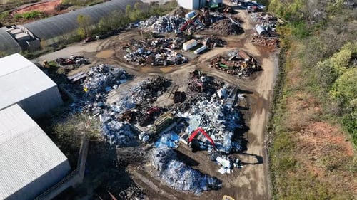 Working excavate on scrapyard on sunny day. Aerial flyover shot. Transporting metal and old scrap