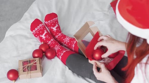 Woman Opening Box of Christmas Ornaments on Bed