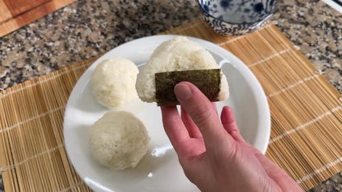 A Hand is Holding a Freshly Made Onigiri Wrapped With Seaweed - Close Up