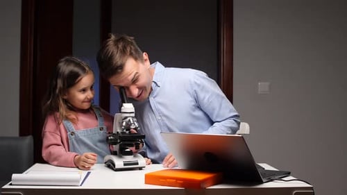 Girl and Man Looking in Microscope in Home