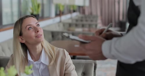 Waiter Talking to Woman Sitting at Table Placing Order in Restaurant Waiter Takes an Order on a